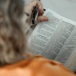 Kobieta czyta Biblię z długopisem, skupiona na wybranym fragmencie